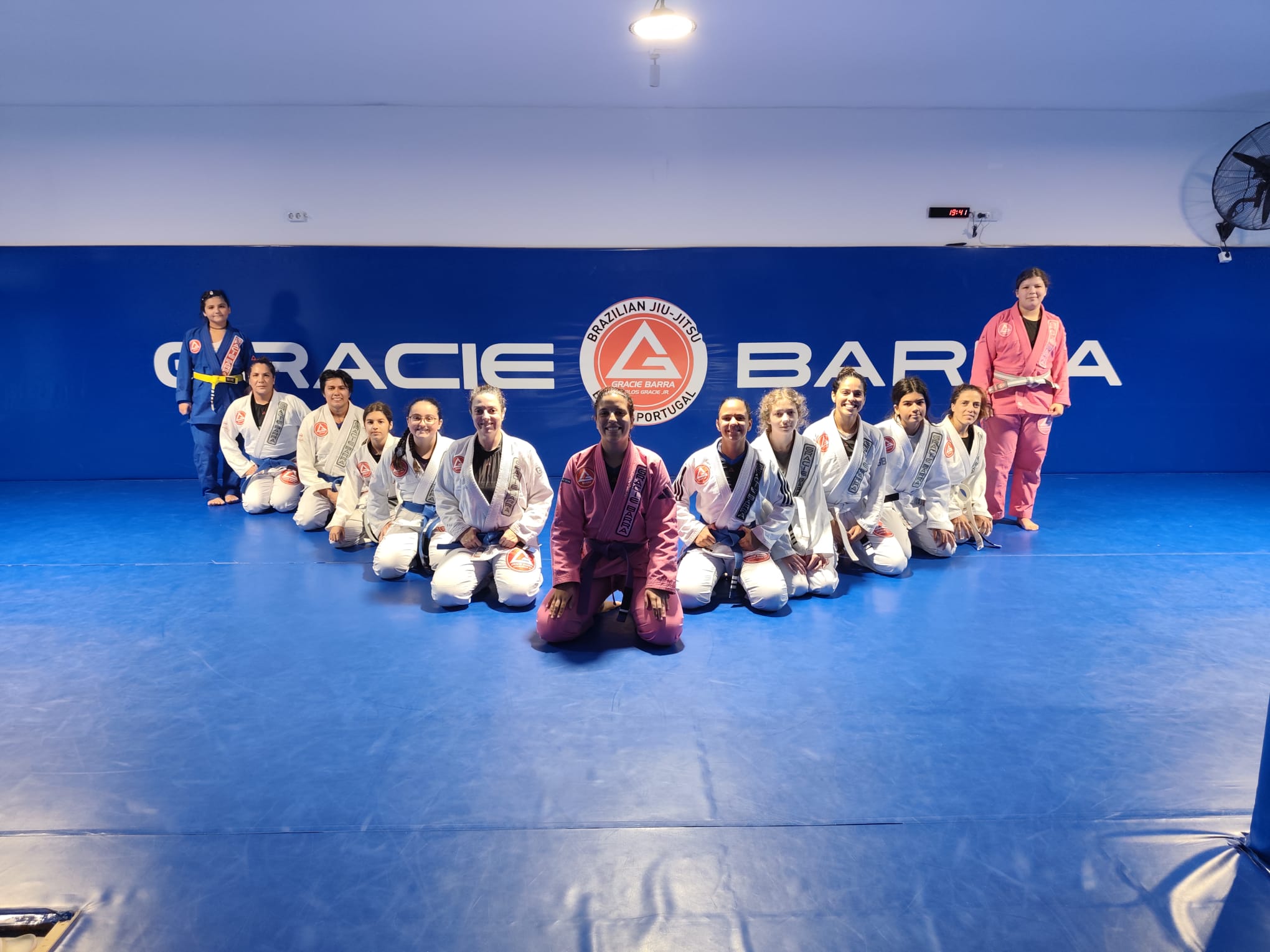 Turma feminina completa da Gracie Barra Braga reunida à frente da parede Gracie Barra