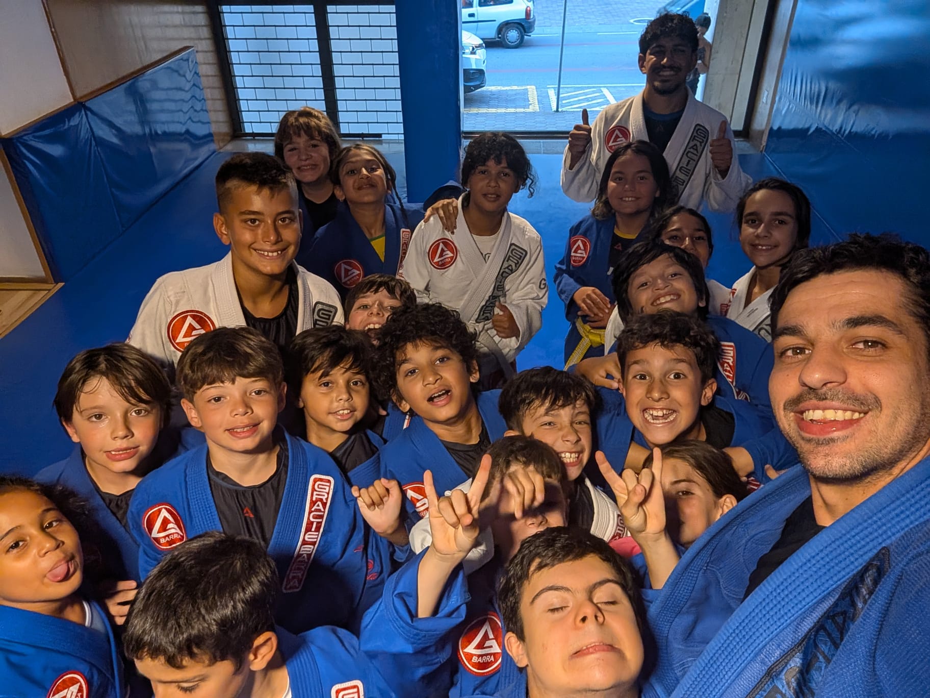 Grupo de crianças e jovens da Gracie Barra Braga sorridentes, à entrada do tatame, a fazer sinal de positivo