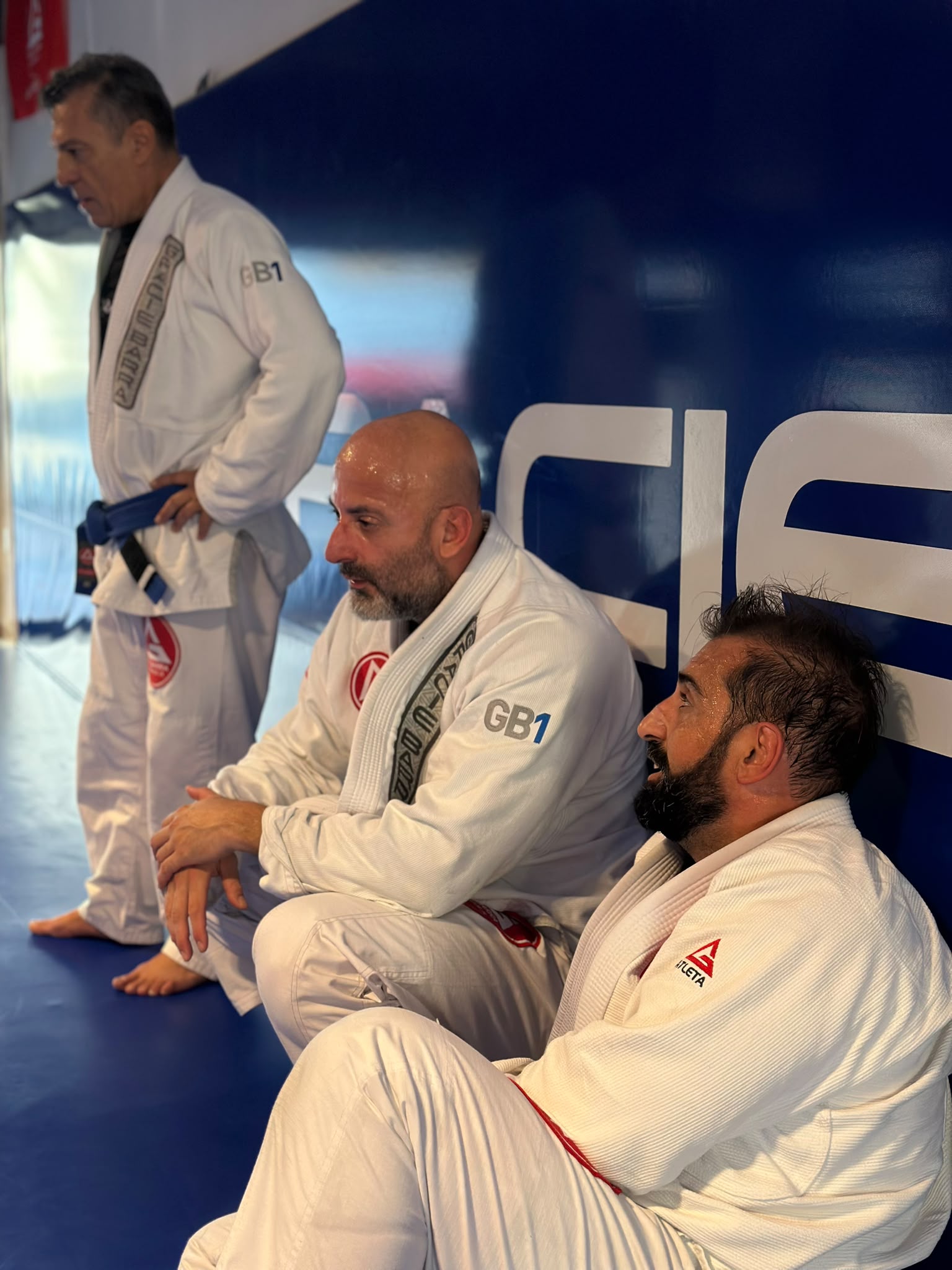 Alunos adultos de kimono branco conversam antes do treino na Gracie Barra Braga